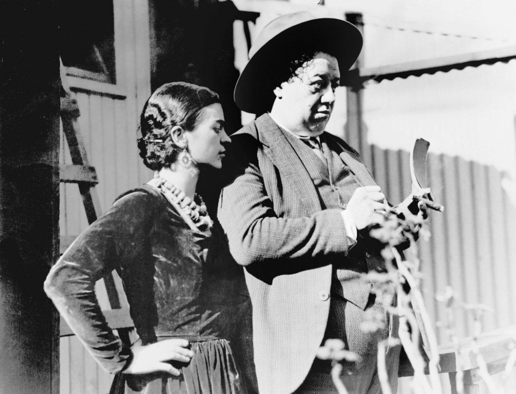 Diego Rivera at work on the Creation mural at Escuela Nacional Preparatoria, watched by Frida Kahlo.